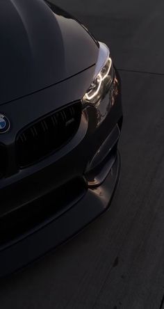 the front end of a black bmw car on a road with its headlights turned down