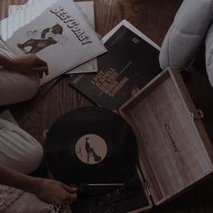 a person is sitting on the floor next to some books and record players in front of them