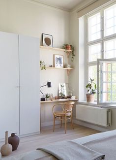 a bedroom with a bed, desk and shelves on the wall next to a window