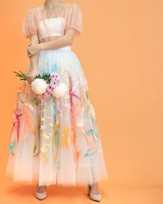 a woman in a dress with flowers on the bottom, and an orange background behind her