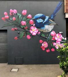 a mural on the side of a building depicts a blue bird perched on a branch with pink flowers