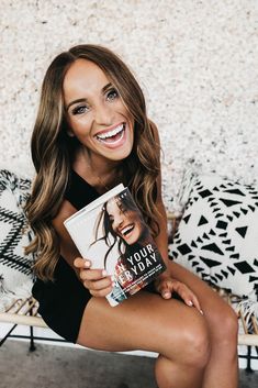 a woman sitting on a couch holding a book in her hand and smiling at the camera