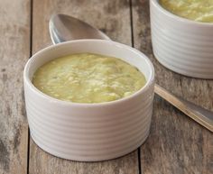 two white bowls filled with green soup on top of a wooden table next to a spoon