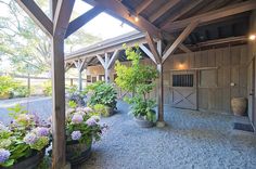 the inside of a barn with lots of plants and flowers in pots on the gravel