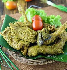 some food is sitting in a wicker basket on a wooden table with green leaves and tomatoes