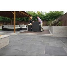 two men are standing in the back yard with an outdoor grill and seating area behind them