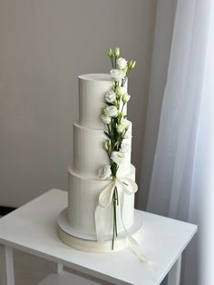 a three tiered white wedding cake with flowers on the top and ribbon around it