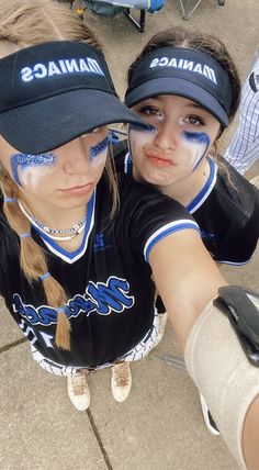 two girls with their faces painted in blue and white baseball uniforms, one is holding her arm around the other's shoulder