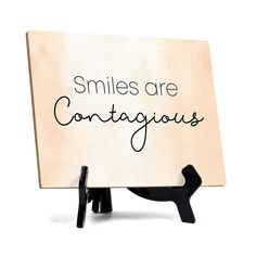 a wooden sign that says smiles are contagious on it with a black cat figurine next to it