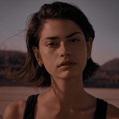 a woman with dark hair wearing a black tank top and looking off into the distance