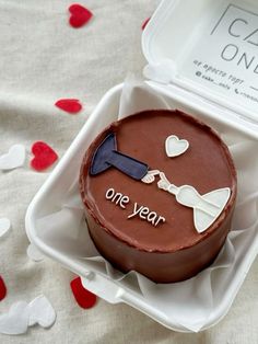 a chocolate cake in a plastic container with one year written on the side and hearts scattered around it