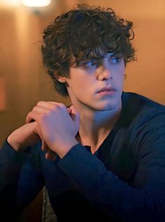 a young man with curly hair and blue eyes is looking at the camera while wearing a black shirt