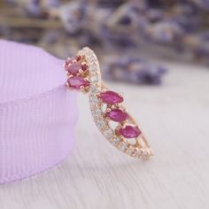 a close up of a pink ring on a white surface with purple flowers in the background