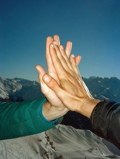 two hands reaching out to each other in front of snow covered mountains and blue sky