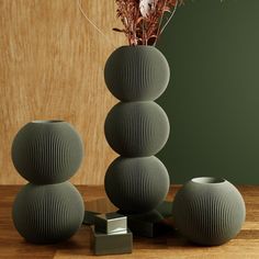 three green vases sitting next to each other on top of a wooden table with flowers in them