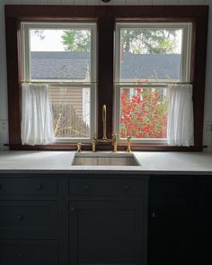 a kitchen sink under two windows in front of a window with curtains on the outside