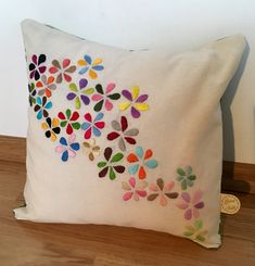 a white pillow with multicolored flowers embroidered on the front and back, sitting on a wooden floor