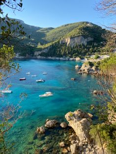 boats are floating in the clear blue water near some cliffs and trees, with mountains in the background