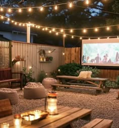 an outdoor movie is set up in the backyard with string lights strung over it and wooden benches