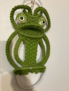 a crocheted frog keychain hanging from a hook on a white wall