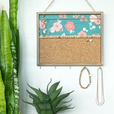 a cork board hanging on the wall next to a potted plant and necklaces