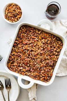 a casserole dish filled with pecans next to two plates and silverware