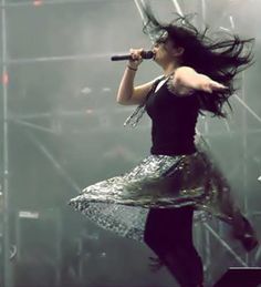 a woman in a black top and skirt on stage with her hair blowing in the wind