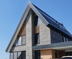 a modern house with an angled roof and wooden shutters on the windows is shown in front of a blue sky