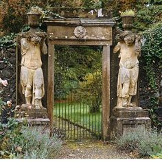 an old gate with statues on it in the middle of some bushes and trees,