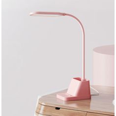 a pink desk lamp sitting on top of a wooden table next to a white wall