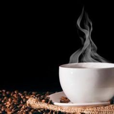 a cup of coffee with steam rising out of it on top of some coffee beans