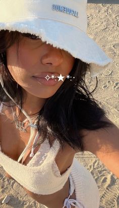 a woman wearing a white hat with stars on the side and one ear piercing is standing in the sand