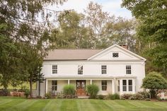 a large white house sitting in the middle of a lush green field with lots of trees