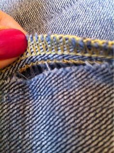 a woman's hand with red nail polish on her nails is stitching the side of a pair of jeans