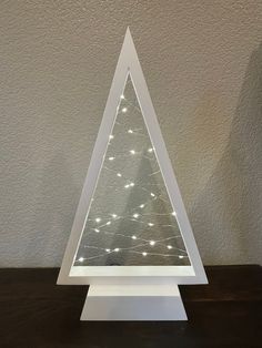 a small white christmas tree with lights on it's sides sitting on a table