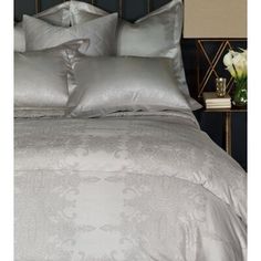 a bed with silver sheets and pillows on top of it next to a night stand