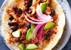 a tortilla topped with meat, onions and avocado