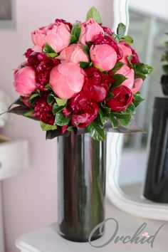 a vase filled with pink and red flowers on top of a white table next to a mirror