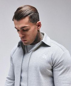 a man with a shaved head and tattoos on his face, wearing a grey jacket