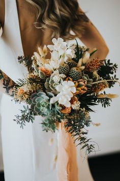 a woman holding a bouquet of flowers in her hands and wearing a white dress with an orange sash