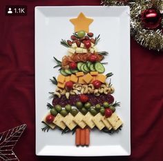 a christmas tree made out of fruits and vegetables on a white plate with red background