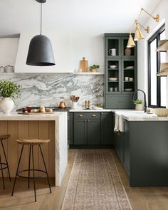 a kitchen with green cabinets and marble counter tops, an area rug on the floor