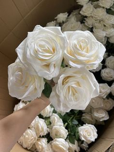 someone is holding white roses in a box