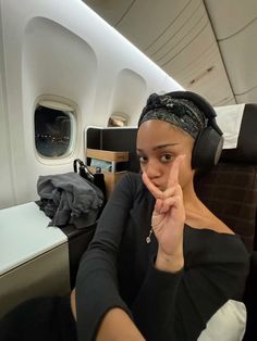 a woman with headphones on sitting in an airplane and pointing to the side while looking at the camera