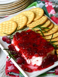 a white plate topped with cheesecake covered in cranberry sauce and crackers