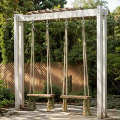 a wooden swing with rope hanging from it's sides in a garden area surrounded by trees