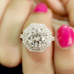 a woman's hand holding a diamond ring with pink nail polish on the other hand