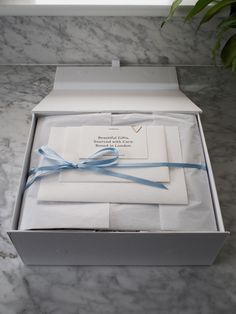 a white box with a blue ribbon and some papers in it on a marble surface