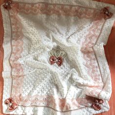 a white crocheted blanket with pink and silver buttons on it sitting on top of a wooden floor