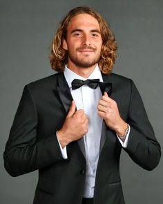 a man in a tuxedo adjusts his bow tie while looking at the camera